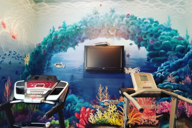 Underwater mural of a coral reef on a home gym wall, with fish, sea turtles, jelly fish, an eel, and an octopus.